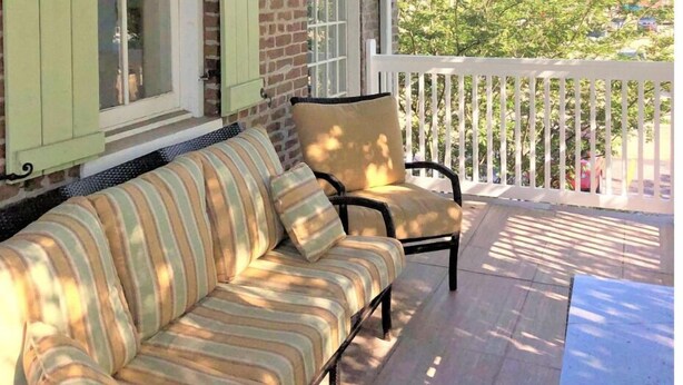 A porch with a striped sofa and a chair, a table, and a view of a brick building with a tower. - Heart of Downtown w Balcony by Dauphin St; walk to restaurants & shops SLEEPS 6! (Mobile)