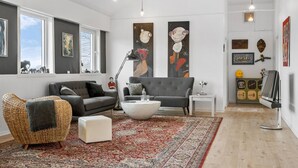 A modern living room with a grey sofa, a wicker chair, a white ottoman, and a red patterned rug. There are two large abstract paintings on the walls, a floor lamp, and a small table with a vase. - Amazing home in Vandel with Wi-Fi (Vandel)