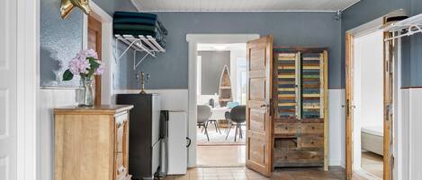 A hallway with a wooden cabinet, a glass vase with flowers, a drying rack, and a surfboard.