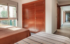 A bedroom with two beds, a wooden wardrobe, and a view of the garden through a window. - 4 bedroom nice home in Cartaya (Cartaya)