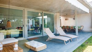 Een overdekt buitengebied met twee lounge fauteuils, een houten tafel en een rieten pouf.