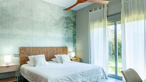 Een moderne slaapkamer met een groot bed, een houten hoofdbord, een nachtkastje met een lamp, en uitzicht op groen buiten het raam.