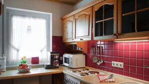 A kitchen with wooden cabinets, a microwave, a stove, and a window with curtains. - Stunning apartment in Winterberg (Winterberg)