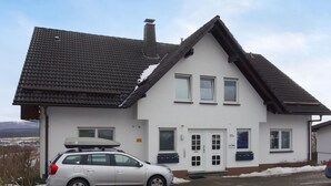 A two-story building with a sloped roof, a car parked in front, and a view of a snowy landscape in the background. - Stunning apartment in Winterberg (Winterberg)