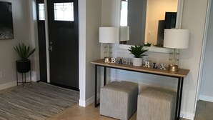 A hallway with a dark door, a console table with decorative items, two striped ottomans, and a mirror above the console table. - Beautiful Home on a canal.  Heated pool.  Sunrise and Sunsets are spectacular. (Cape Coral)