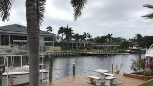 A marina with boats docked, a wooden deck with a table and chairs, and palm trees. - Beautiful Home on a canal.  Heated pool.  Sunrise and Sunsets are spectacular. (Cape Coral)