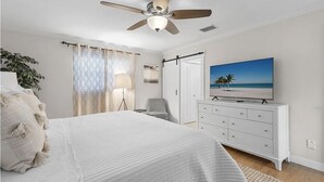 A bedroom with a bed, a ceiling fan, a TV, a dresser, a chair, and a window with curtains. - Beautiful Home on a canal.  Heated pool.  Sunrise and Sunsets are spectacular. (Cape Coral)