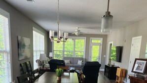 Eine moderne Küche mit Marmorarbeitsplatte, ein Essbereich mit einer Couch und Stühlen sowie große Fenster mit Jalousien.
