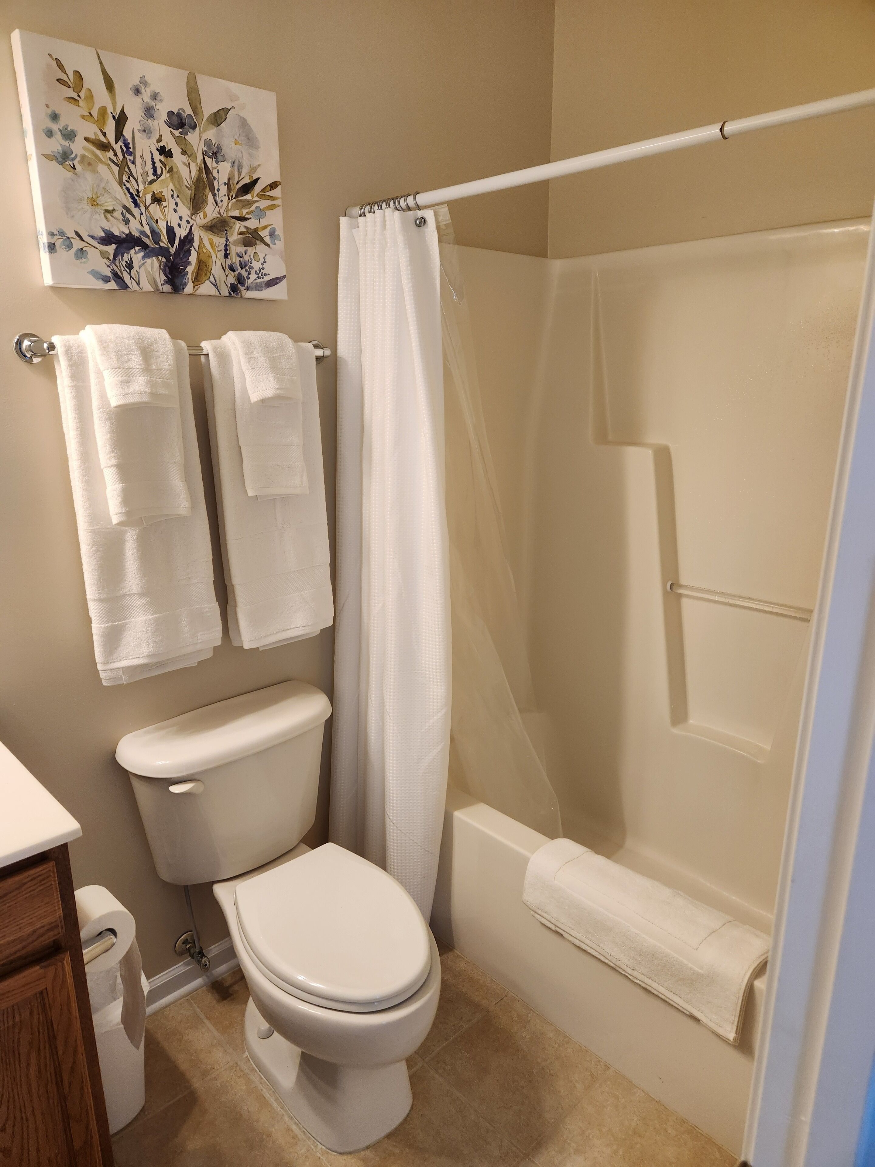 A bathroom with a toilet, shower, and two towels hanging on the wall.