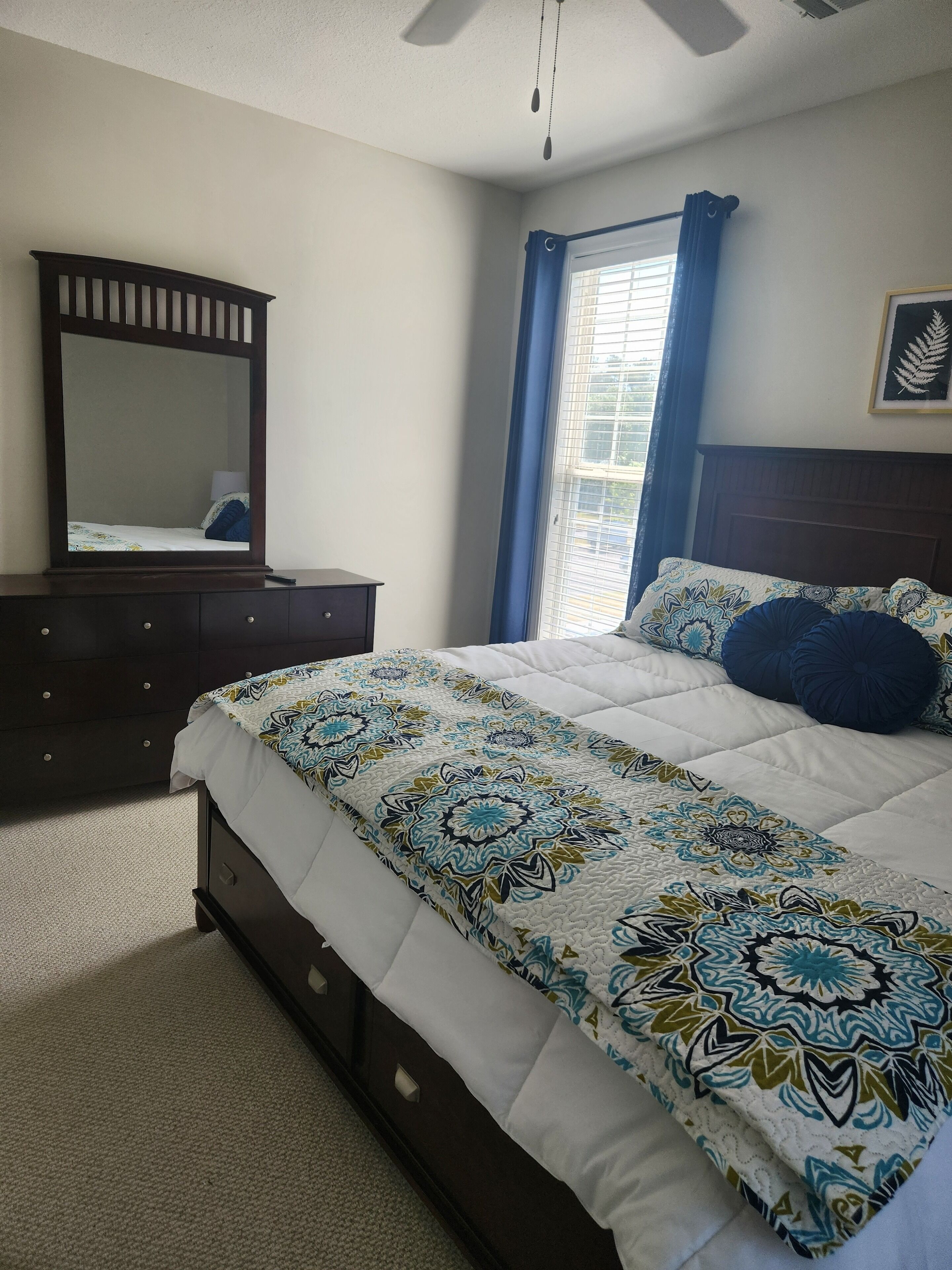 A bedroom with a bed, a dresser, a mirror, and a window with curtains.
