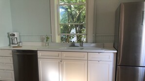 A kitchen with white cabinets, a stainless steel refrigerator, a dishwasher, and a window with a view of trees. - Sweet Cozy Victorian in Housatonic. Close to everything.  (Housatonic)