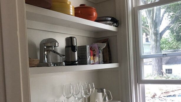 A kitchen with white shelves containing various kitchenware, a kettle, and a window with a view of trees and a building outside. - Sweet Cozy Victorian in Housatonic. Close to everything.  (Housatonic)