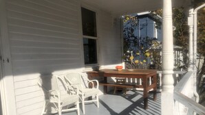 A porch with a wooden table and two wicker chairs, a small stool, and a window with blinds. - Sweet Cozy Victorian in Housatonic. Close to everything.  (Housatonic)