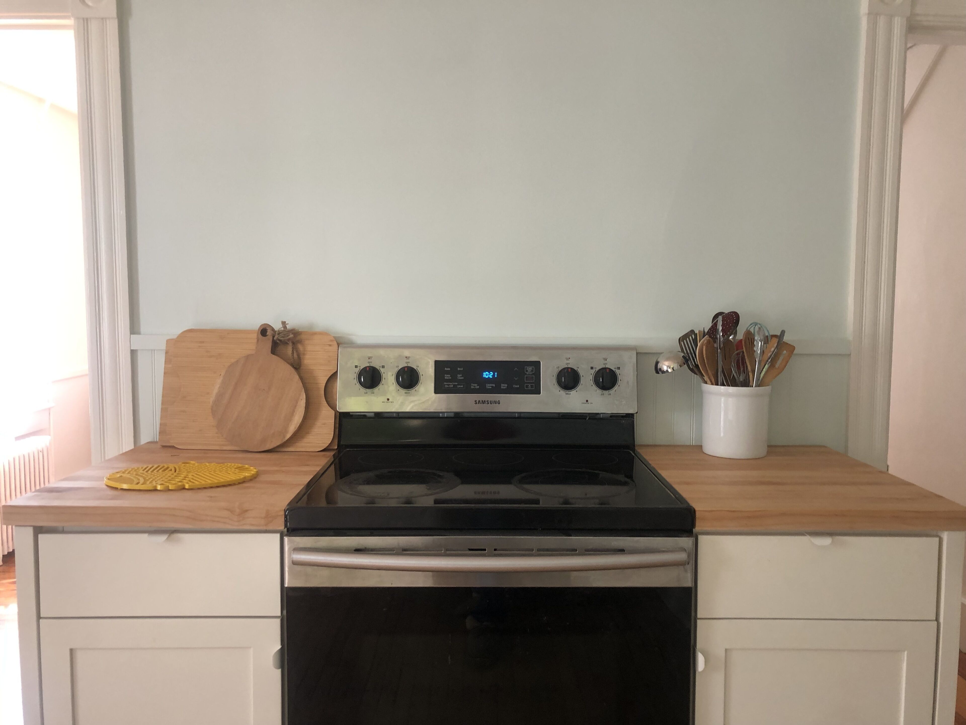 A kitchen with a Samsung stove, wooden cutting board, and a utensil holder.