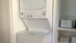 A compact laundry room with a front-loading washer and dryer, a microwave, and a shelf with stacked plates. - Sweet Cozy Victorian in Housatonic. Close to everything.  (Housatonic)