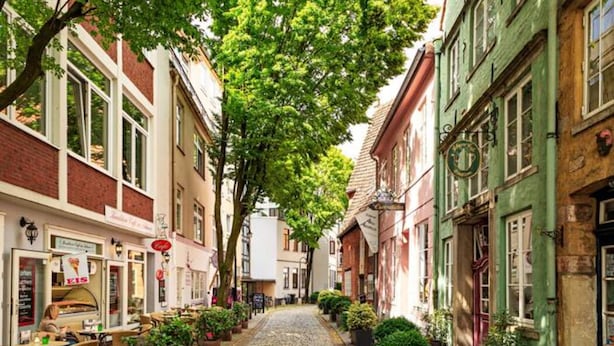 A cobblestone street lined with traditional European buildings, some with outdoor seating and potted plants. - Gemütliche Wohnung in Leipzig Zentrum mit Terrasse (Leipzig)