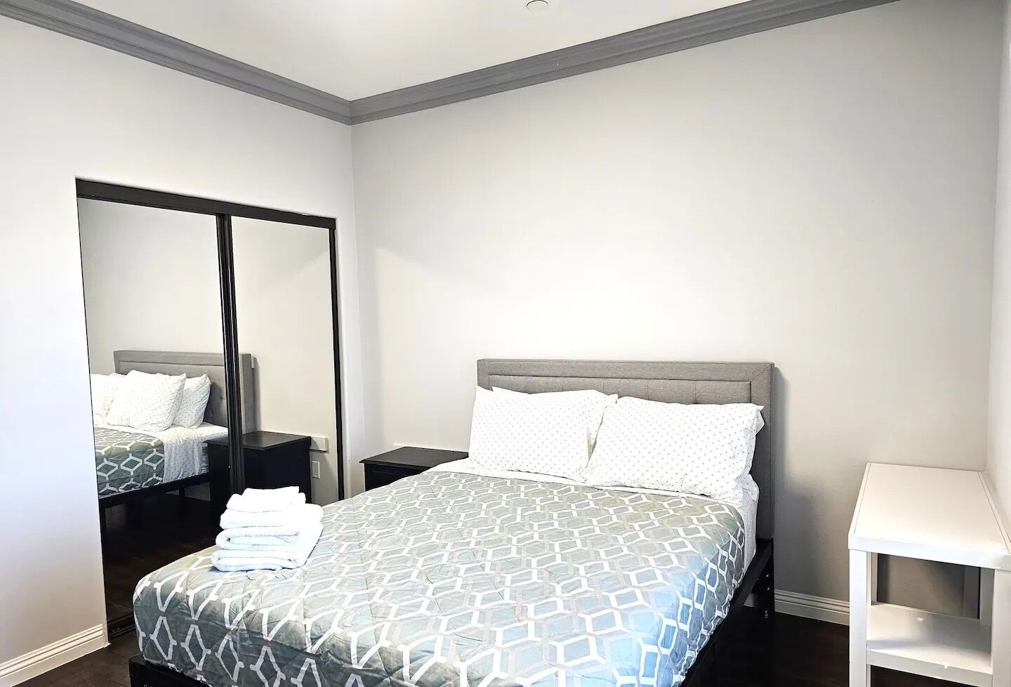 Une chambre d’hôtel moderne avec un grand lit, une table de chevet, une commode, un miroir et une petite table blanche.