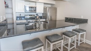 A modern kitchen with white cabinetry, stainless steel appliances, a granite countertop, and bar stools. - BIG DISCOUNTS ON ALL MONTHLY RENTALS  - EXLARGE FACING  Emerald Coast Gulf Front (Panama City Beach)