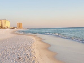 A beach with a sandy shore and ocean waves. There are buildings in the background.