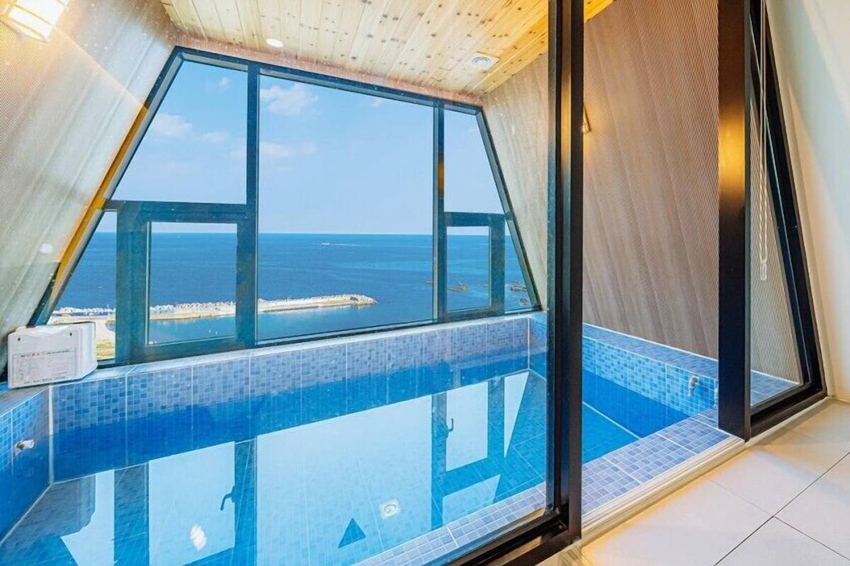 A room with a large window overlooking a pool and the sea.