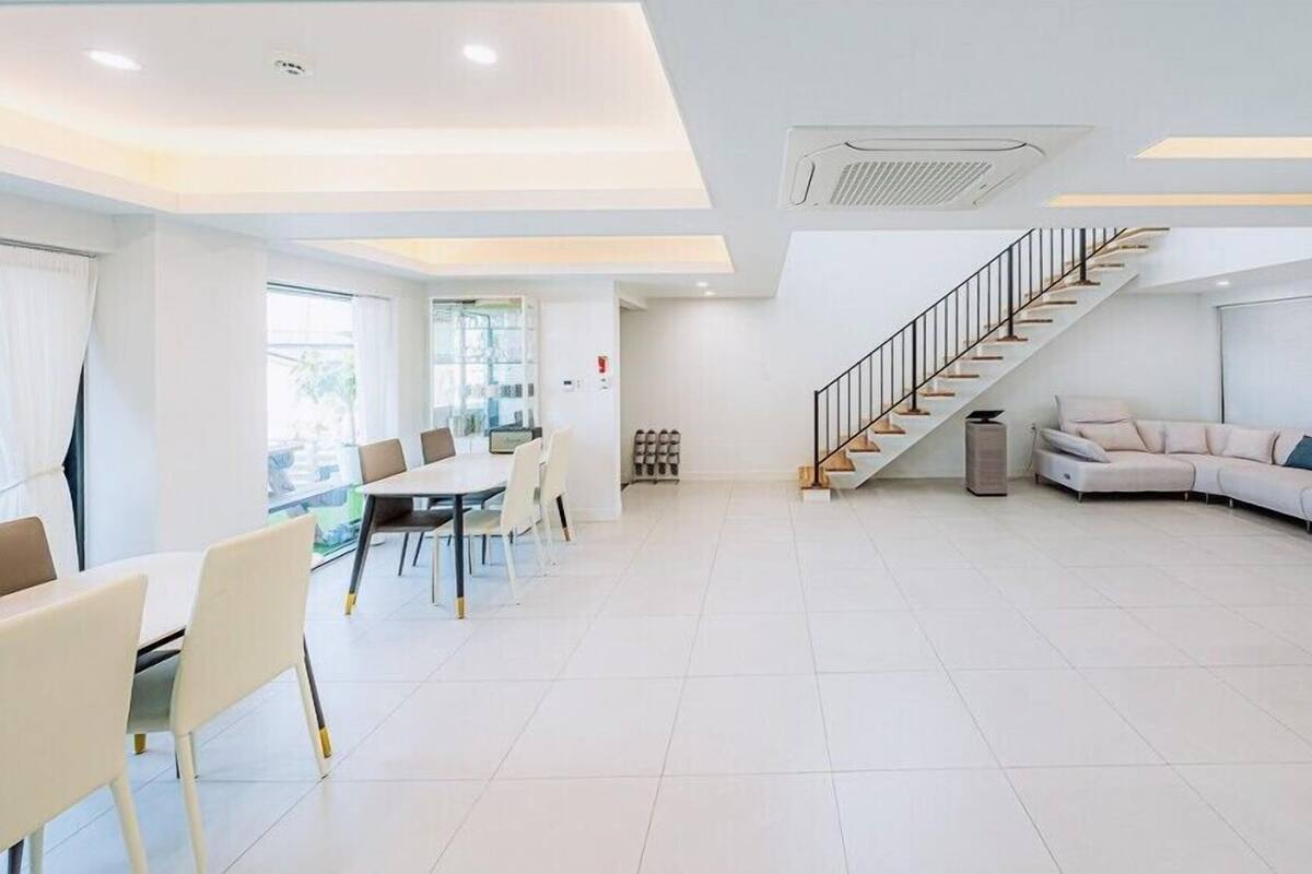 A spacious living area with a modern staircase, a dining table with chairs, and a large sofa.