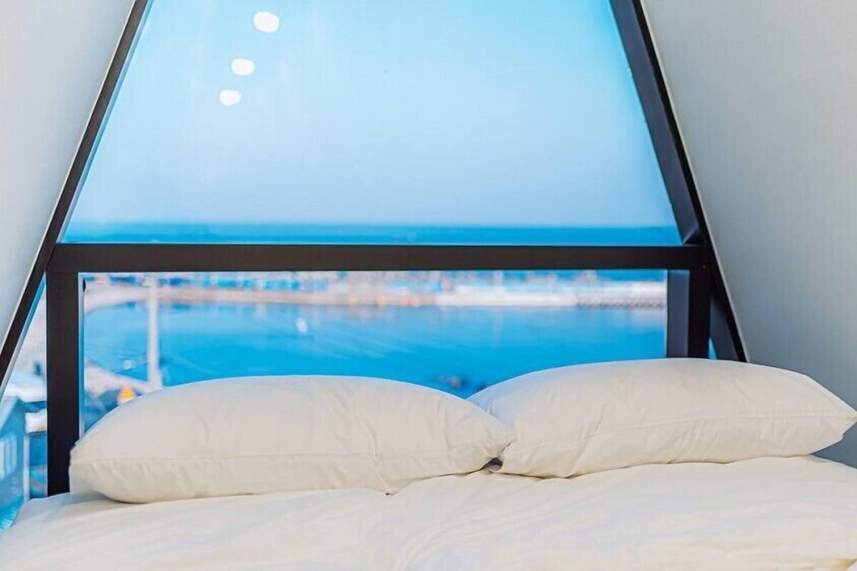 A bed with white bedding in a room with a view of the sea through a triangular window.