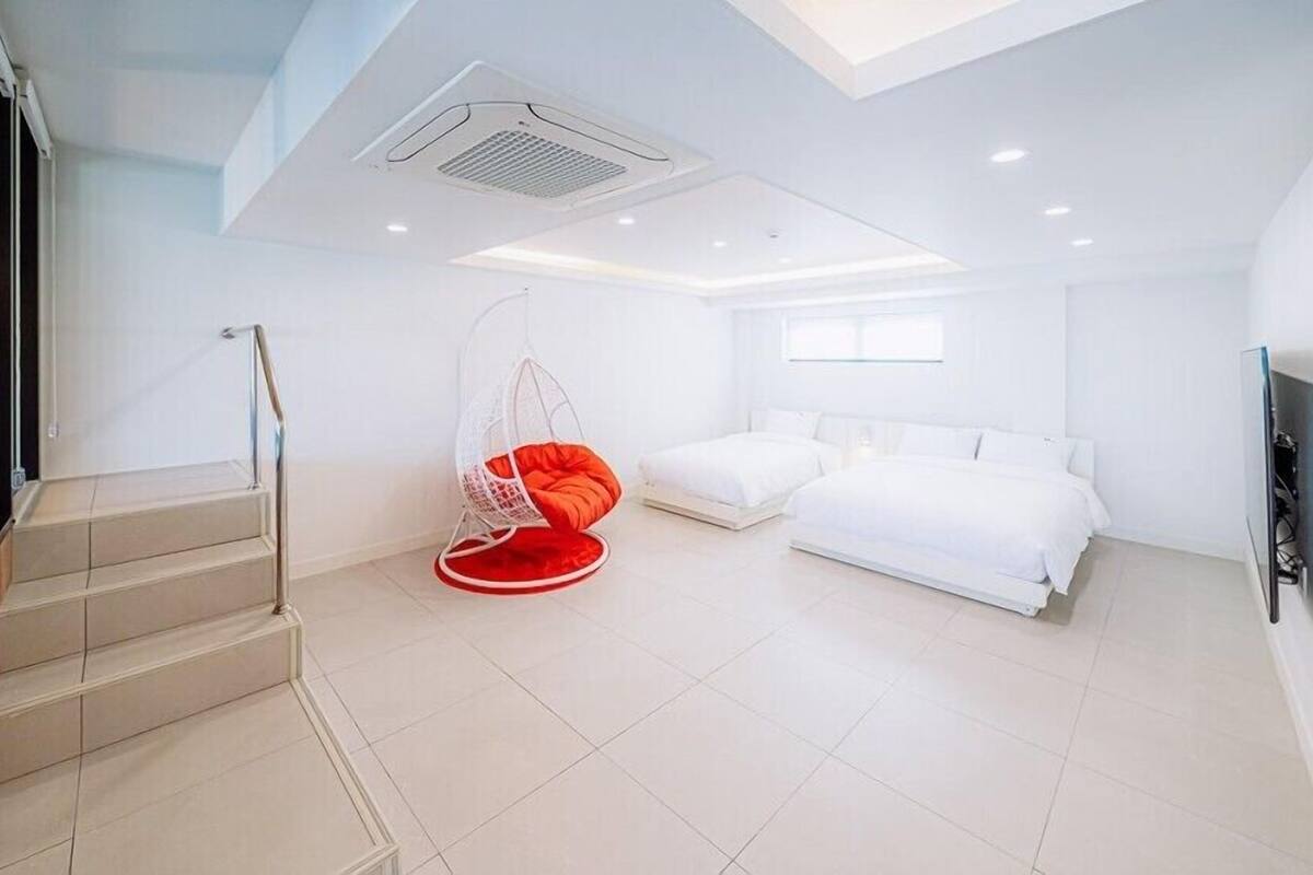 A modern hotel room with a staircase, a hanging chair, a bed, and a TV.
