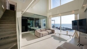 Uma sala de estar moderna com uma TV grande, um sofá e vista para o oceano.