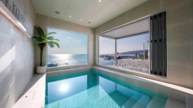 Piscina interior moderna com vista clara para o mar e paisagem costeira.