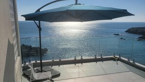 Uma varanda com vista para o mar, guarda-corpo de vidro e uma cadeira.