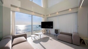 Uma sala de estar espaçosa com uma televisão grande, assentos confortáveis e vista para o oceano.