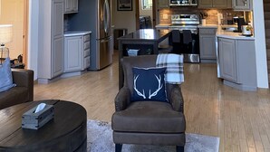 Een ruime loft-achtige woonruimte met een hoge plafond, een houten trap, een keuken met moderne apparatuur en een gezellige zithoek met een comfortabele fauteuil en een kleine tafel.