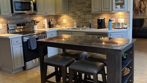 Een moderne keuken met een centraal eiland, donkerhouten krukken en een backsplash van steen.