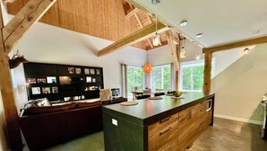 Une cuisine moderne dotée d’un grand îlot central, de poutres en bois et d’une bibliothèque intégrée.