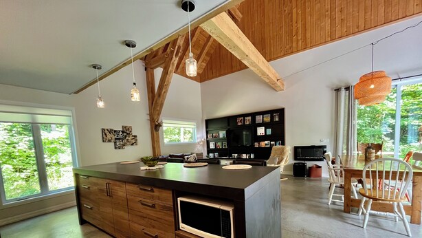 Une cuisine moderne dotée d’un grand îlot central, de meubles en bois, d’un éclairage suspendu et d’un coin repas offrant une vue sur la verdure.