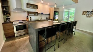 Une cuisine moderne dotée d’un îlot central, d’appareils électroménagers en acier inoxydable et de tabourets de bar.