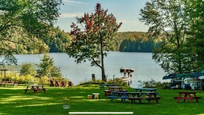 Un espace de pique-nique au bord du lac, avec des tables et des chaises, une jetée où se trouvent des personnes, et une rangée de bateaux.