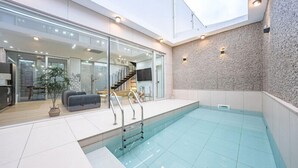 A modern indoor swimming pool with a glass wall, a stone wall, and a staircase leading to an upper level. - Stay 13 Wol (Gyeongju)