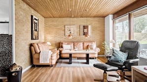 A modern living room with a brick wall, wooden ceiling, and large windows.