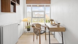 A modern interior with a wooden-framed table, a chair with a fur throw, a potted plant, and a window with a view of houses.