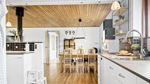 A modern kitchen with wooden flooring, a dining area with a wooden table and chairs, and a kitchen island with a sink and countertop.