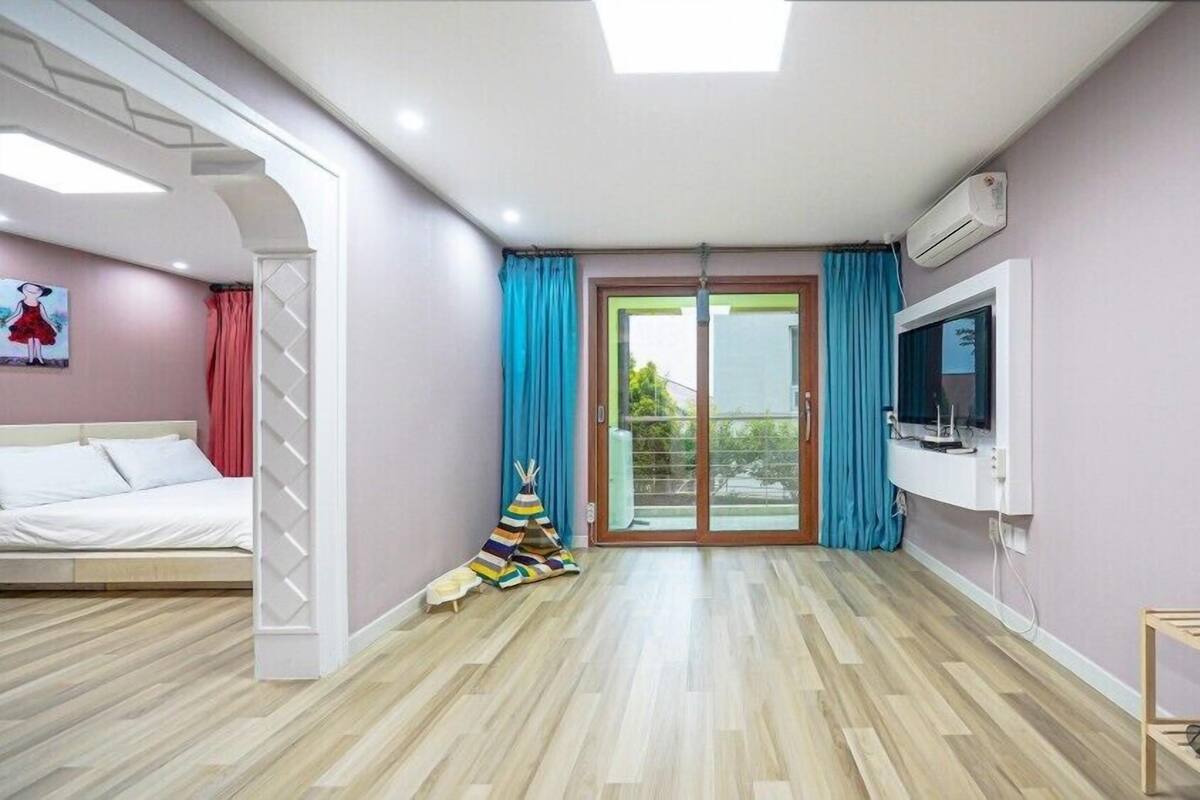 Un dormitorio moderno con cama, televisor y puerta corrediza de vidrio que da a un balcón.