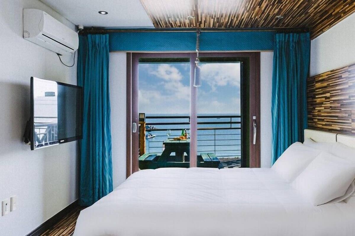 Habitación de hotel con cama, televisor, balcón con mesa y sillas, y vista al mar.