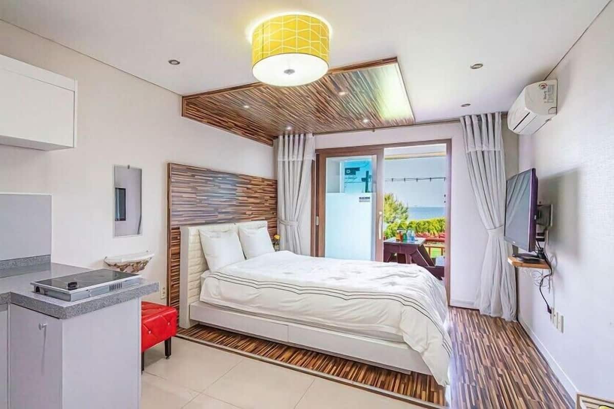 Habitación de hotel moderna con cama, una kitchenette pequeña, un televisor y un balcón con vistas.