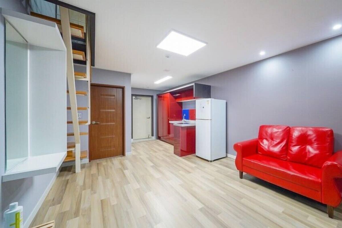 Un apartamento moderno con piso de madera, sofá de cuero rojo, kitchenette y escalera.