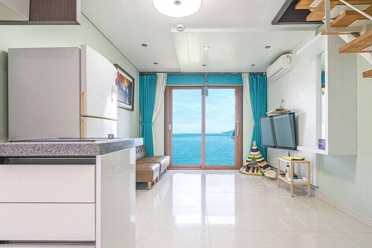 Una cocina moderna con refrigerador empotrado, un comedor con banco, televisión y vista al mar a través de un ventanal.