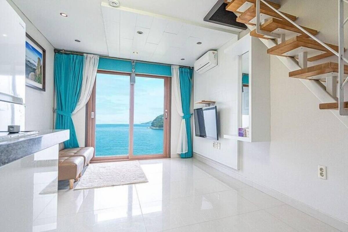 Un salón moderno con vistas al mar, una escalera de madera y un televisor de pantalla plana.
