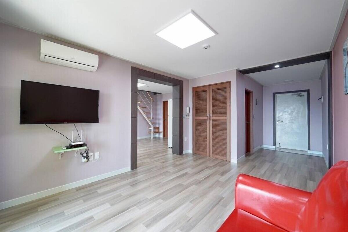 Una sala de estar moderna con una televisión de pantalla plana, un sofá rojo y una escalera que conduce a otro nivel.