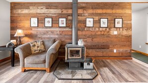 A cozy room with a wooden wall, a sofa, a table with a lamp, and a wood-burning stove. - Stunning views, Strong Wi-fi, and Private Beach! (Lilliwaup)