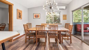 A dining area with a wooden table and chairs, a chandelier, and a large window with a view of trees. - Stunning views, Strong Wi-fi, and Private Beach! (Lilliwaup)